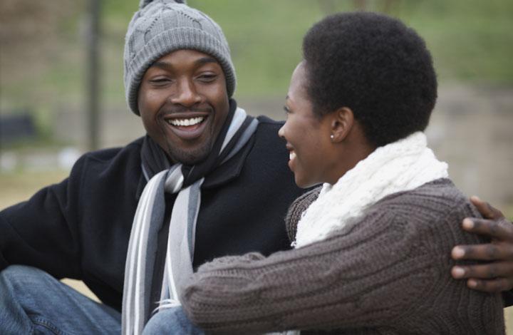 Black man with arm around black lady, both smiling