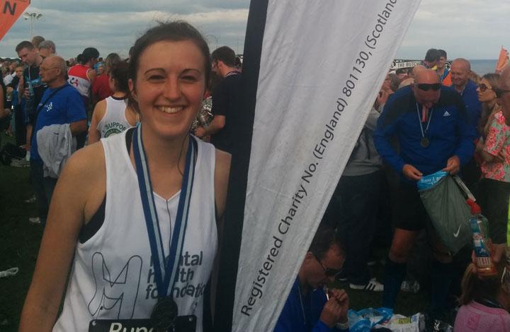 Female runner with medal posing with banner