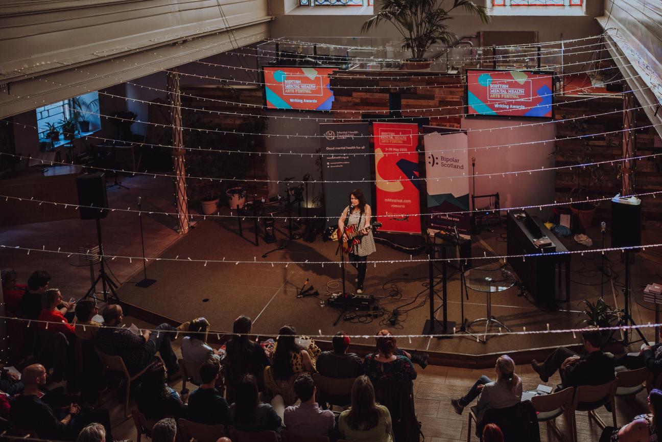 Photo of a woman performing in front of a large crowd, at the Scottish Mental Health Arts Festival 2019