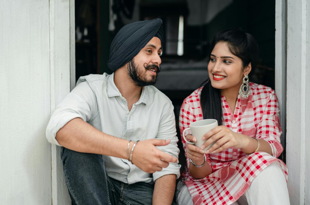 An Indian man and woman sitting chatting as she holds a cup of tea