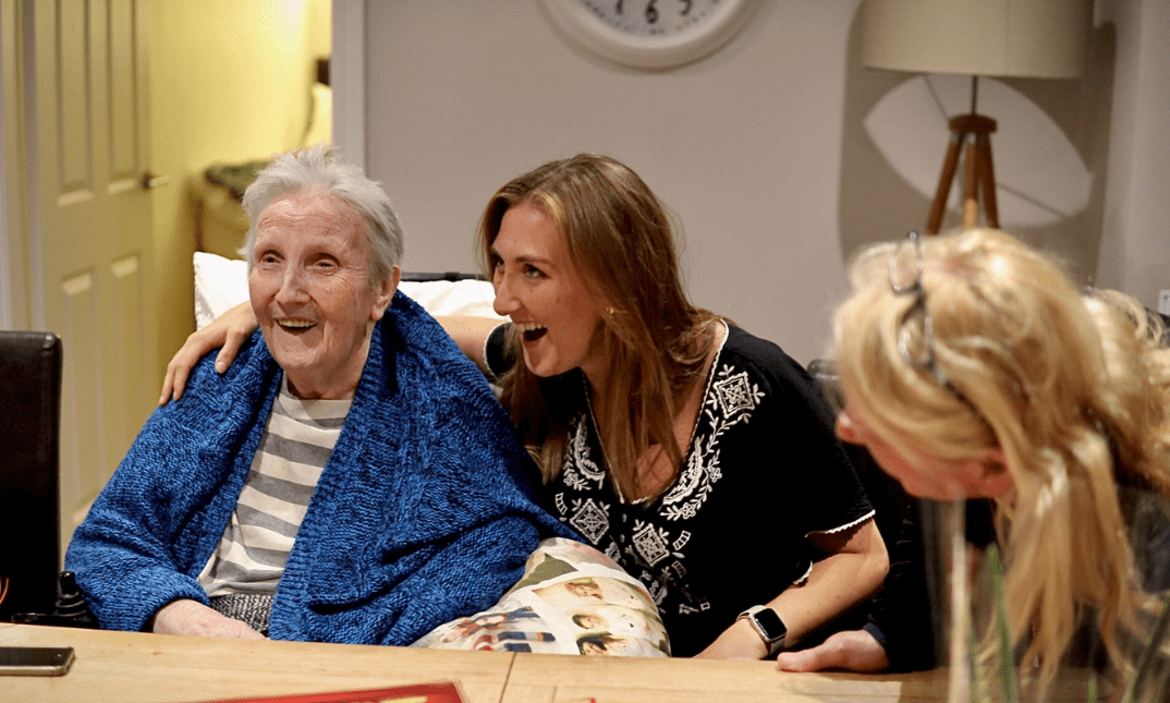 3 women of mixed ages are sat talking cheerfully at a table.