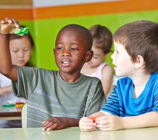 Children playing together, sat at desks