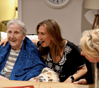 3 women of mixed ages are sat talking cheerfully at a table.