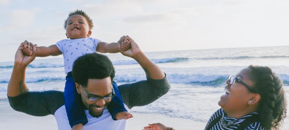 Man with baby on shoulders and lady laughing on the beach