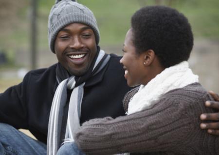 Black man with arm around black lady, both smiling