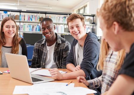 A group of smiling students sitting around a table in a college library talking