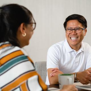 Man smiling and drinking coffee with a friend